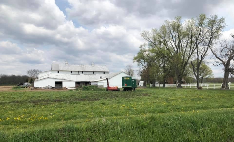 Photo reference for a Watercolor painting of - Baumgardner Homestead, New Carlisle, Ohio. White barn with a green tractor on a grassy field under a cloudy sky.