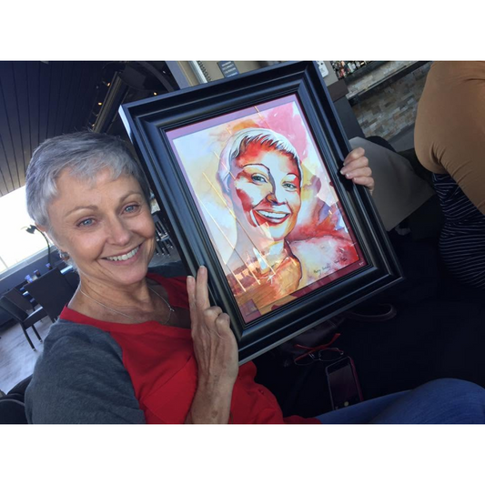 Woman holding a framed watercolor painting of a smiling face in a colorful frame.